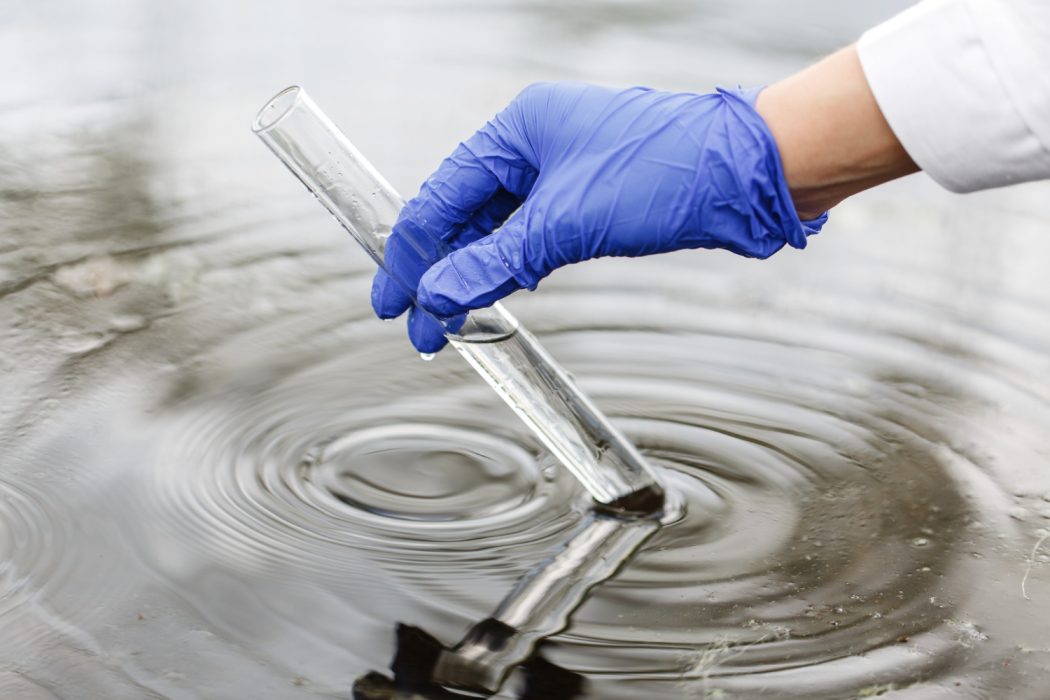 Le chercheur tient un tube à essai avec de l'eau dans une main dans un gant bleu